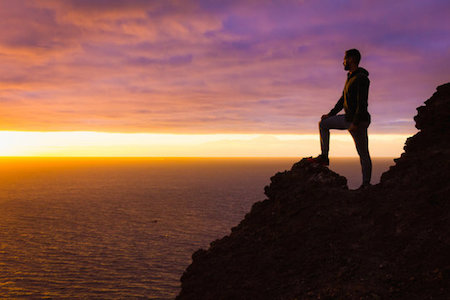 man standing on mountain edge looking at a sunset